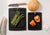 Up close detail of the All-in-One Cutting Board Set in Slate ready for meal prep with fresh asparagus and peppers ready to be expertly chopped with a Victorinox Swiss Modern Chef's knife with wood handle